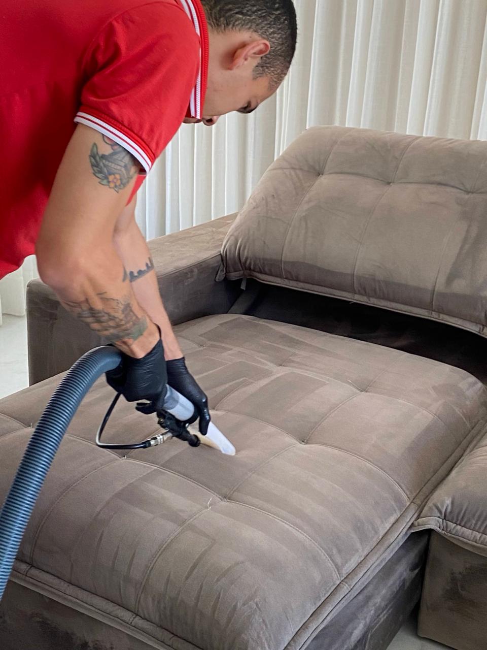 Profissional uniformizado higienizando sofá com equipamento de extração